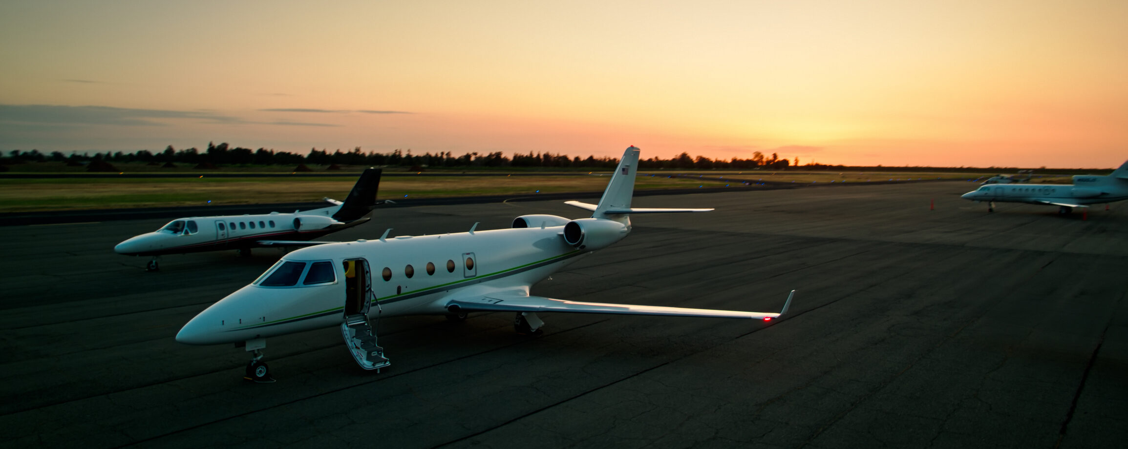 Private jets parked on an airfield at sunset, the nearest with its airstair open